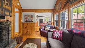 Ein gemütliches Blockhaus mit Kamin aus Stein, Holzwänden, einer Sitzecke mit Sofa und Kissen sowie einer Küche im Hintergrund.