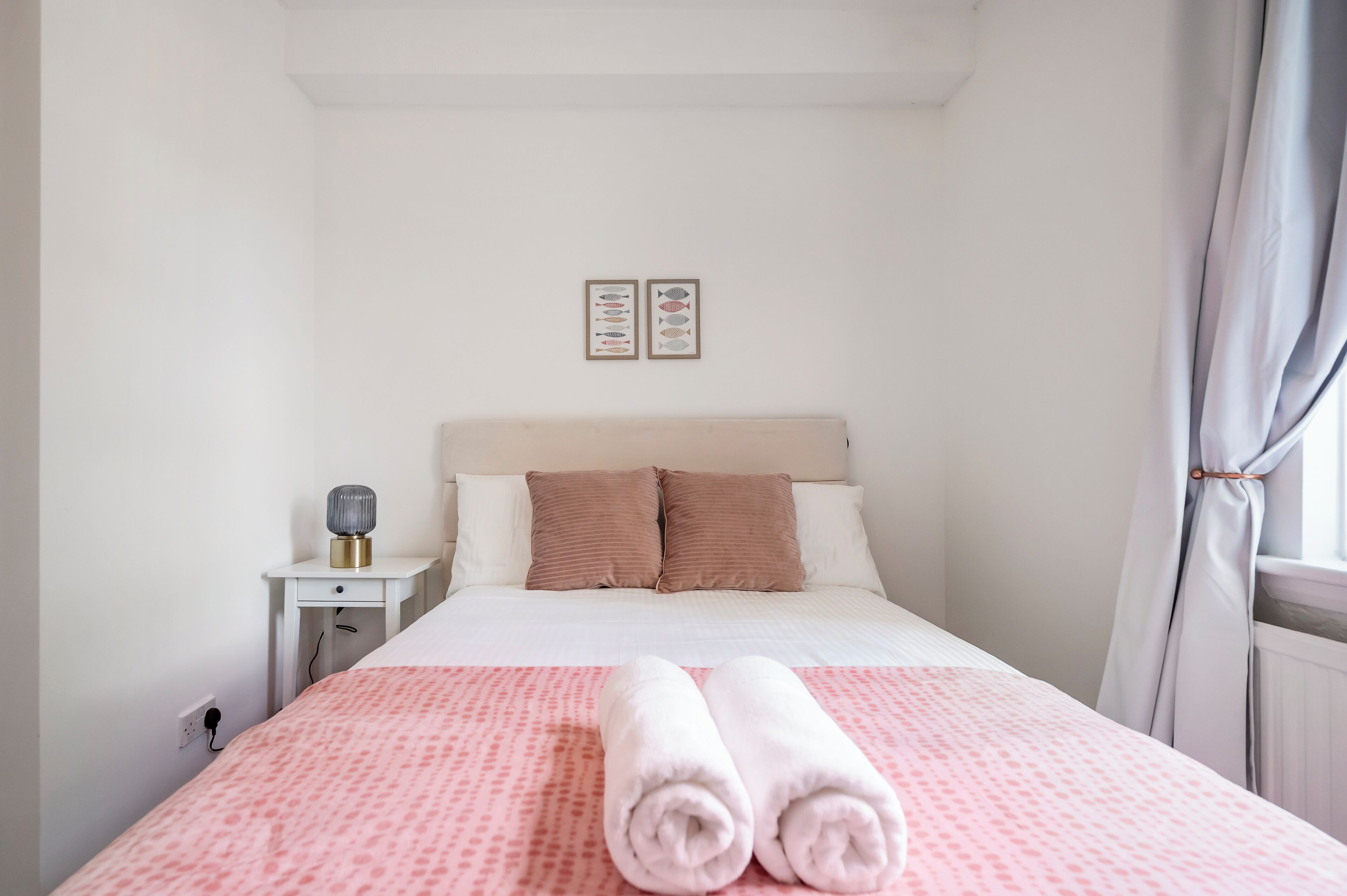 A bedroom with a bed, pillows, a bedside table with a lamp, and a window with curtains.