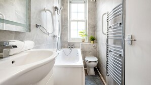 A modern bathroom with a bathtub, shower, toilet, and a window providing natural light. - Modern London stay near Nothing Hill (London)