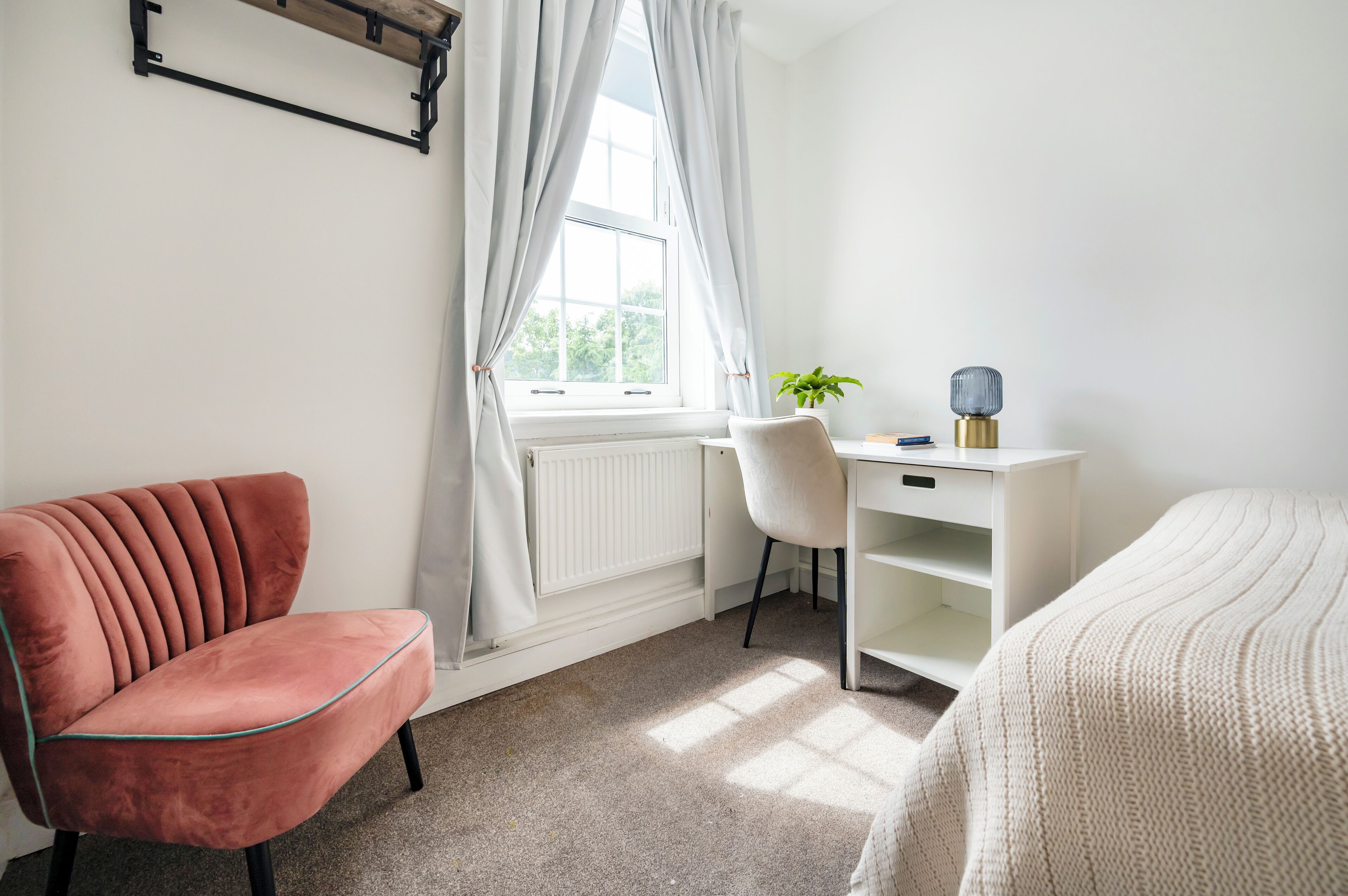 A bedroom with a bed, a desk, a chair, and a radiator.