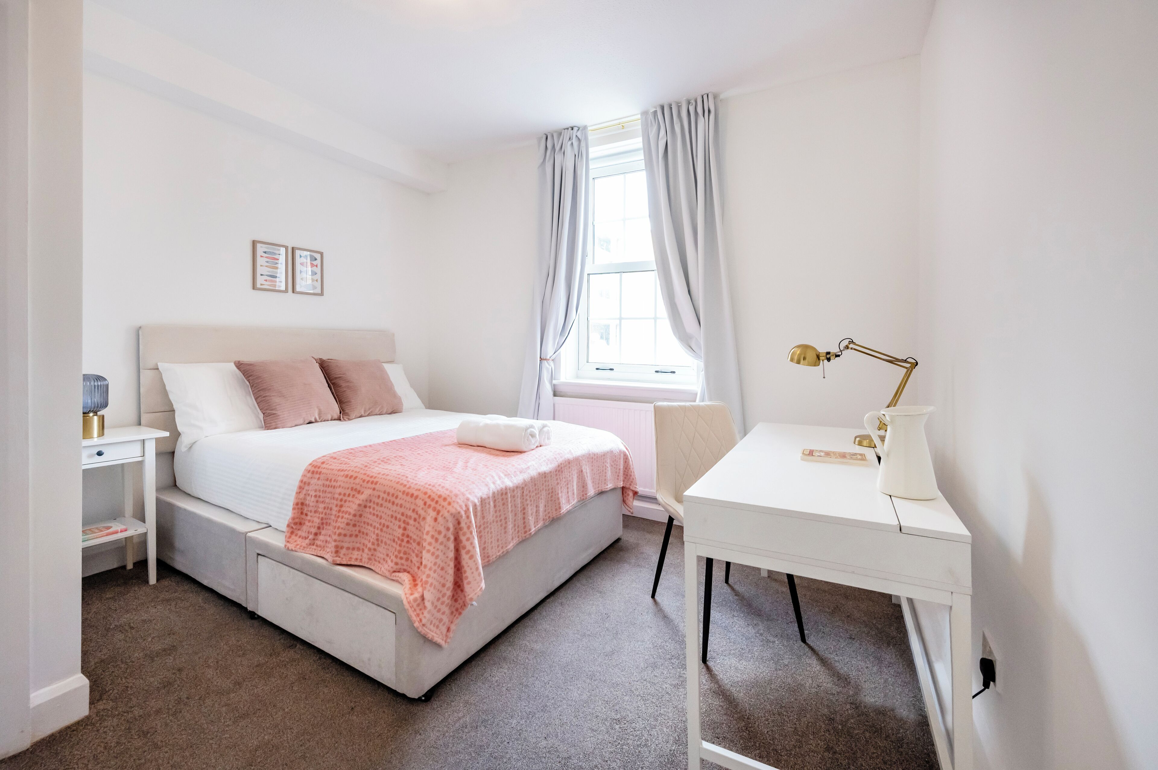 A bedroom with a bed, bedside table, lamp, and window with curtains.