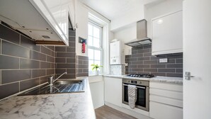 A modern kitchen with dark tiled walls, a marble countertop, a gas stove, and a built-in oven. - Modern London stay near Nothing Hill (London)