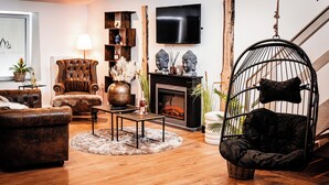 A cozy living room with a fireplace, a hanging chair, and a television mounted on the wall. - Wellness for two (Ahlen)