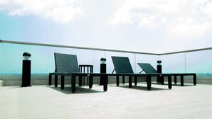 Eine Dachterrasse mit Glasgeländer, mehreren Liegestühlen und einem Tisch.