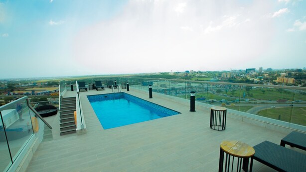 Ein Pool auf dem Dach mit Blick auf die Stadt, einer Glasbrüstung und Sitzgelegenheiten im Freien.