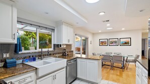A modern kitchen with white cabinets, granite countertops, and a dishwasher. There is a dining area with a table and chairs.