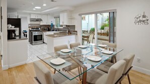 A modern kitchen with white cabinets, stainless steel appliances, and a glass dining table set for six.