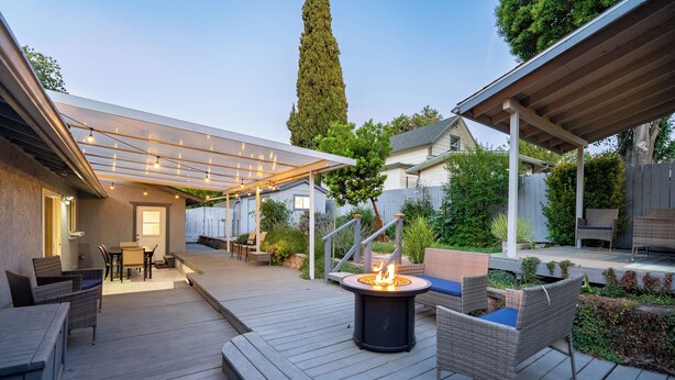 A covered outdoor patio with a fire pit, seating, and a pergola with string lights.