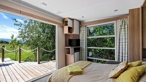 Un dormitorio con una cama grande, un televisor y vistas a un paisaje verde a través de amplios ventanales.