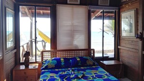 A bedroom with a bed, wooden headboard, and a view of the beach through large windows. - Beachfront Cabin With Wi-fi (Tolú)