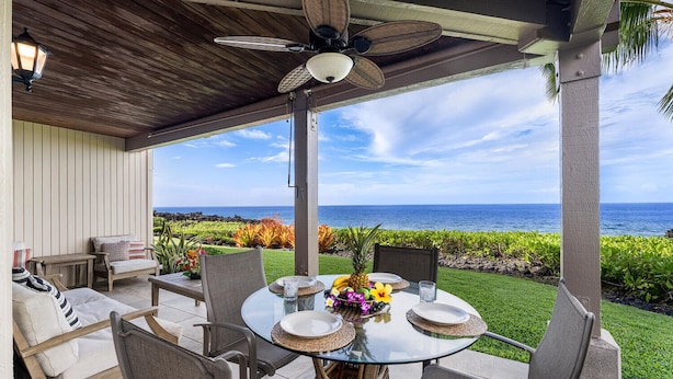 A covered outdoor dining area with a glass table, chairs, and a ceiling fan. - KKSRC#1-101 Direct Oceanfront, Best North Ground Floor Corner, Remodeled, AC! (KAILUA KONA)