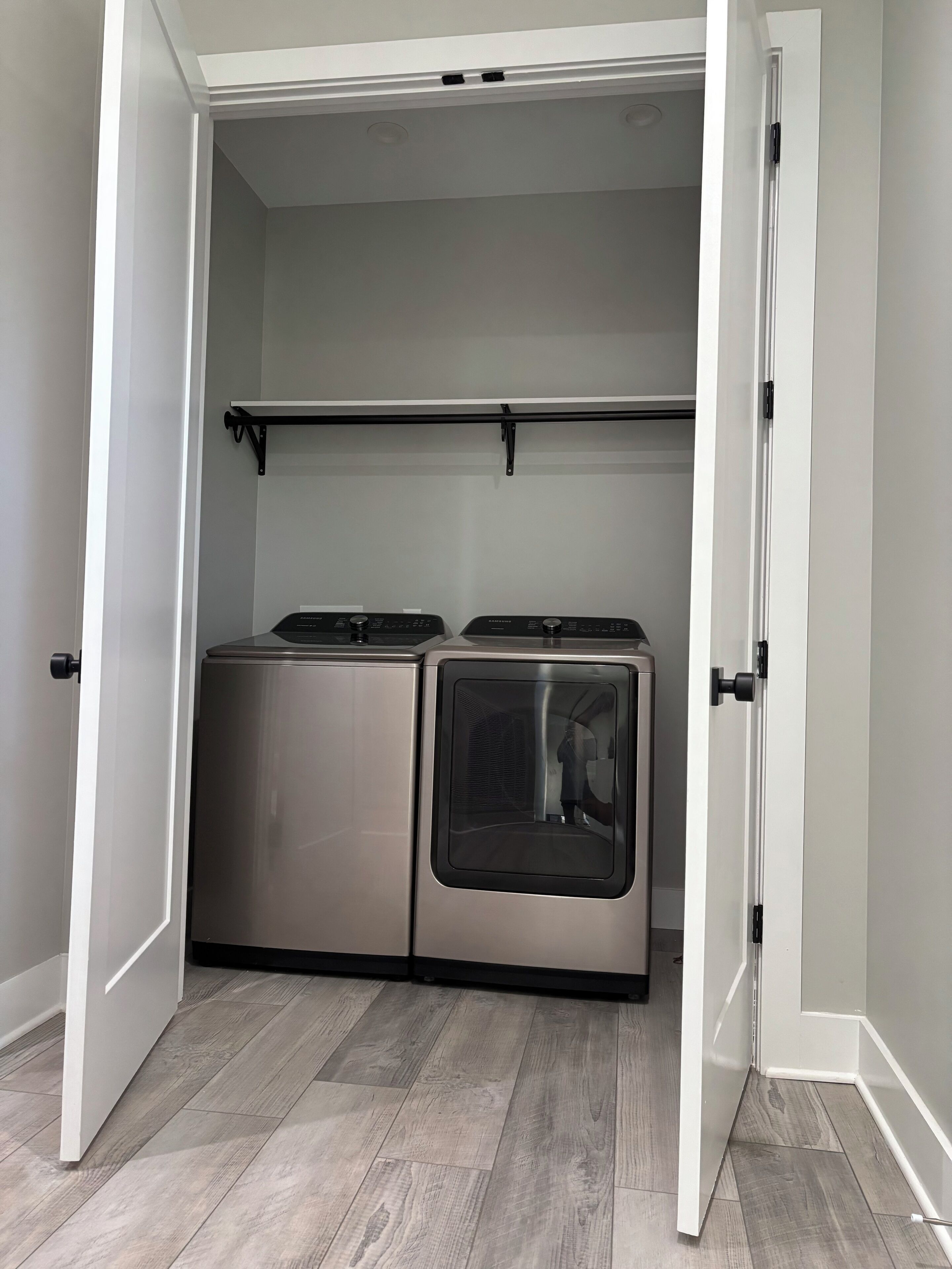 A laundry room with two stainless steel appliances, a drying rack, and a white door.