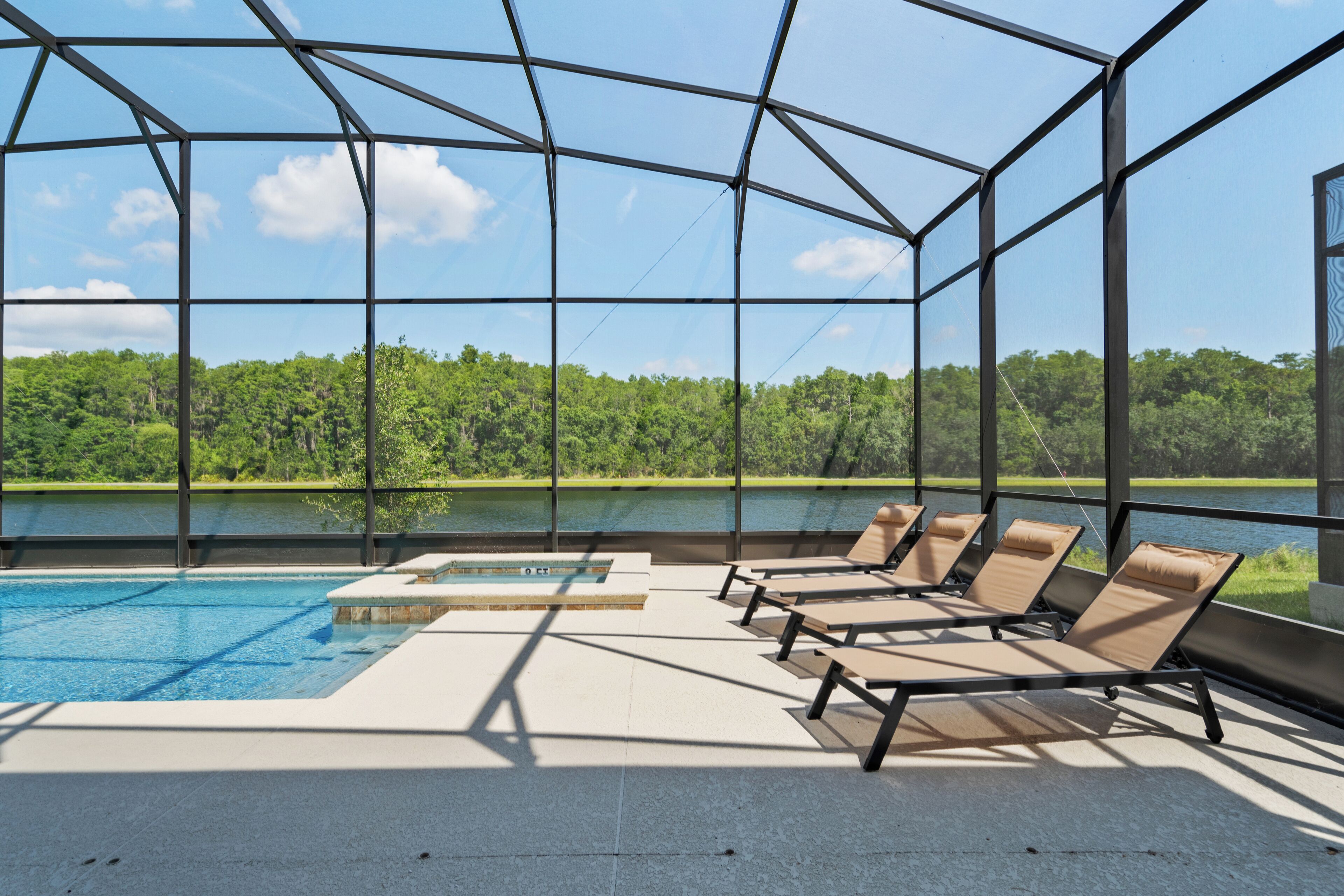 A pool area with lounge chairs and a view of a lake and forest.