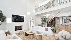 Un vaste espace de vie doté d’une cheminée, de canapés blancs, d’une table basse et d’un escalier menant à un niveau supérieur.