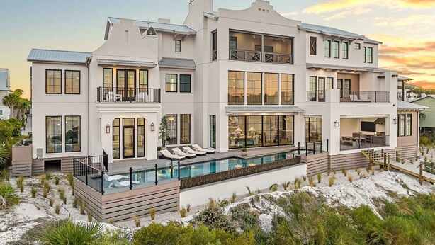 Une maison à plusieurs étages dotée d’une grande piscine, de balcons et située en bord de mer.