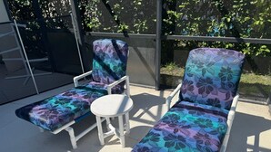 A patio area with two lounge chairs and a small table, surrounded by a glass enclosure with a view of greenery. - Charming 4-bedroom villa with WiFi, AC in wonderful Kissimmee (Kissimmee)