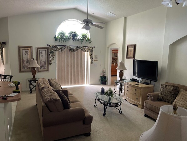 Una sala de estar con sofá, mesa de centro, televisor y plantas decorativas.