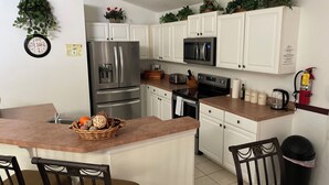 A kitchen with white cabinets, stainless steel appliances, a microwave, a toaster, and a coffee maker. There are chairs and a table in the dining area. - Charming 4-bedroom villa with WiFi, AC in wonderful Kissimmee (Kissimmee)