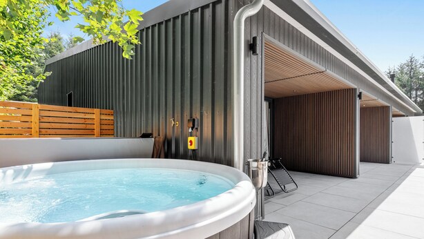 Ein moderner Außenbereich mit Whirlpool, einer Holzterrasse, einem Metallzaun und einem Gebäude mit einer Holzschalung.