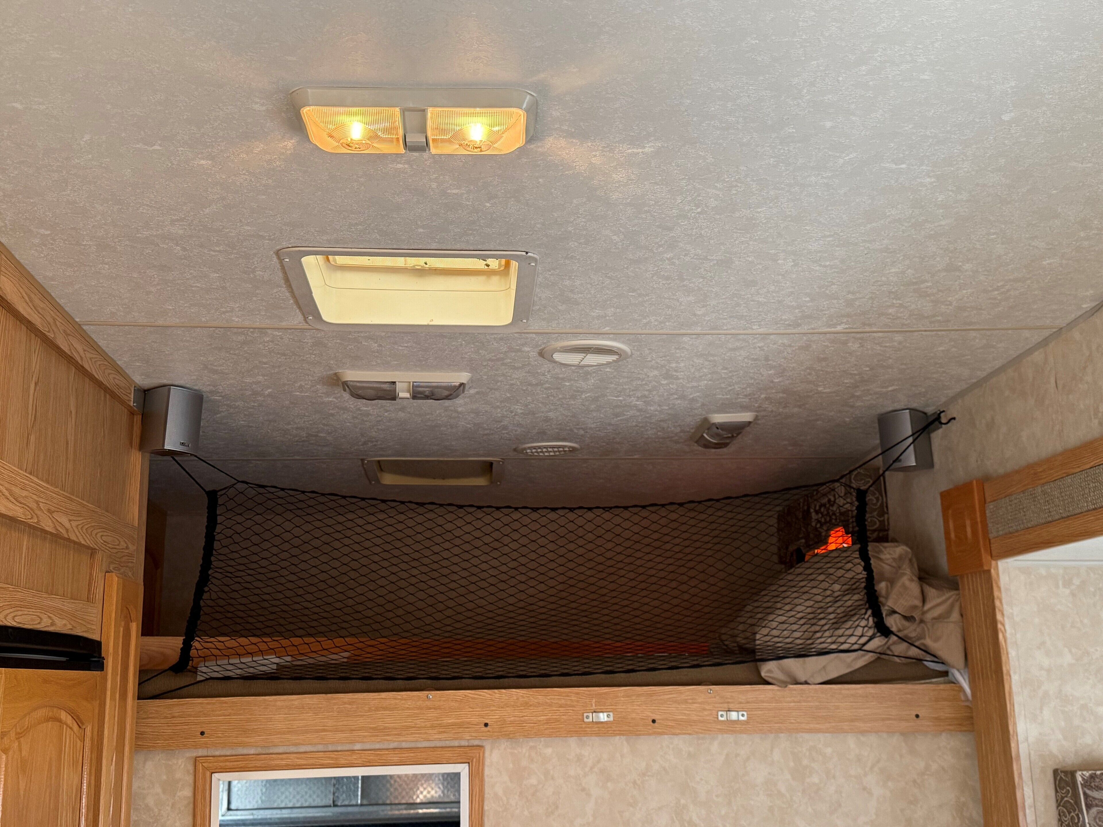 Interior compacte d'una autocaravana amb una llitera, il·luminació al sostre i una petita finestra.