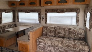 Ein kompaktes Wohnmobil-Interieur mit Küchenzeile, Essbereich und einer Sitzecke mit gemusterten Polstern.