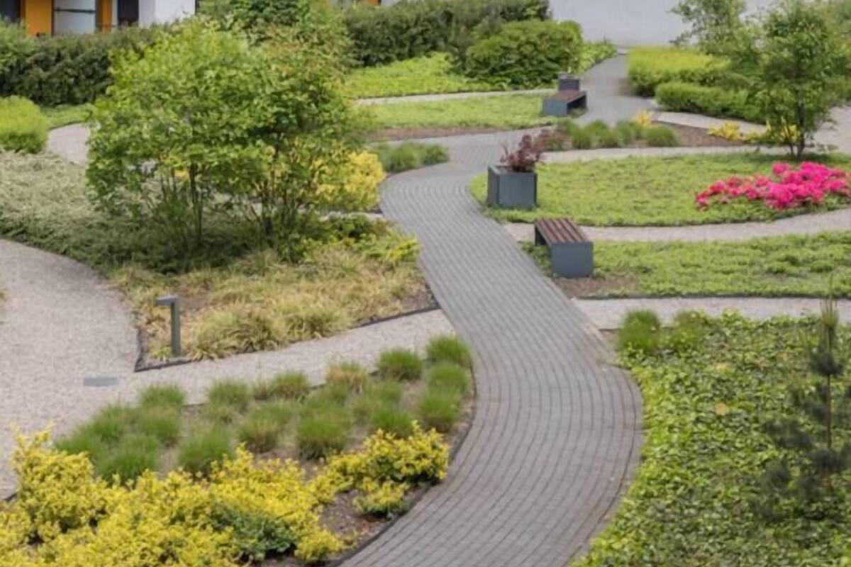 A multi-story residential building with balconies, a landscaped courtyard with pathways, and a variety of plants.