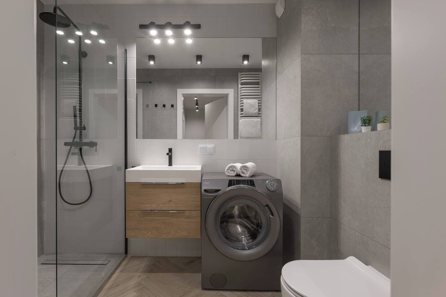 A modern bathroom with a glass shower enclosure, a built-in sink, a washing machine, and a toilet.