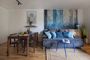 A modern living room with a dining area, a sofa with blue cushions, a coffee table, and a painting on the wall. - Cityscape by Fragola Apartments (Kraków)
