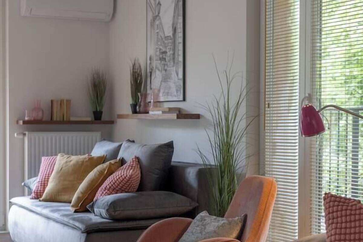 Una sala moderna con un sofá gris, un sillón naranja y una mesa de centro de vidrio.