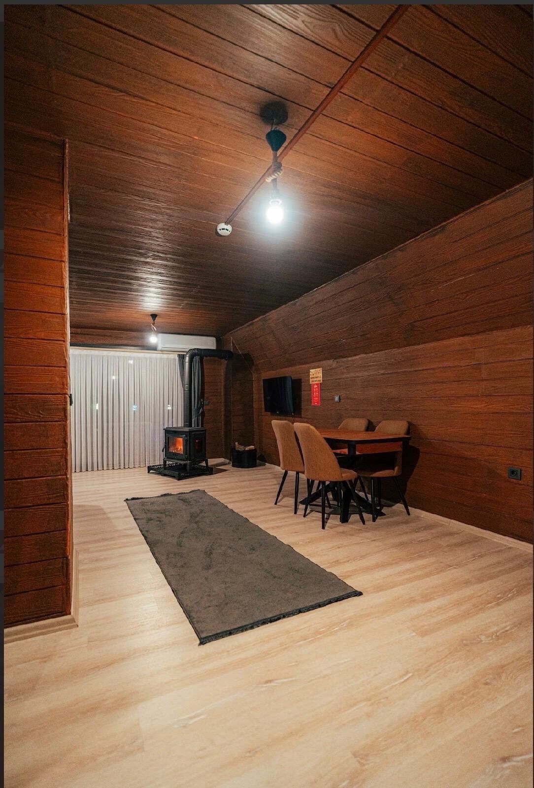 Um quarto de sótão aconchegante com teto de madeira, lareira, mesa de jantar com cadeiras e um tapete grande.