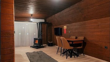 Um quarto de sótão aconchegante com teto de madeira, lareira, mesa de jantar com cadeiras e um tapete grande.