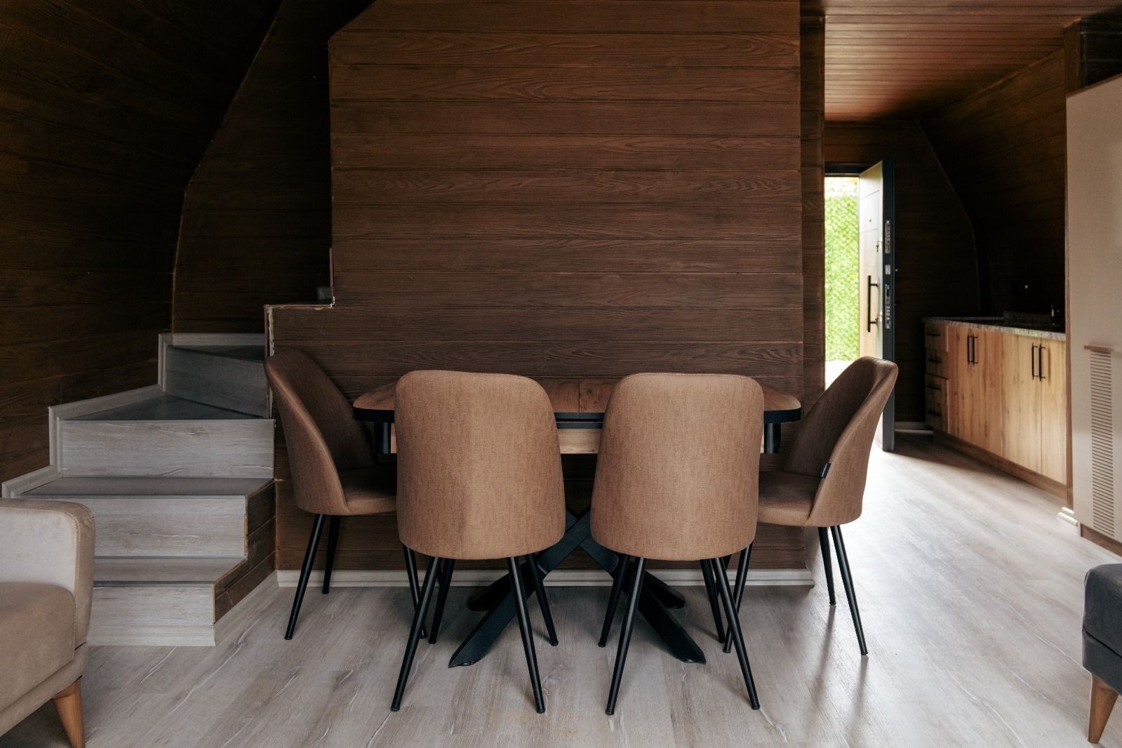 A dining area with a wooden table and four chairs, a staircase, and a kitchen visible through an open door.