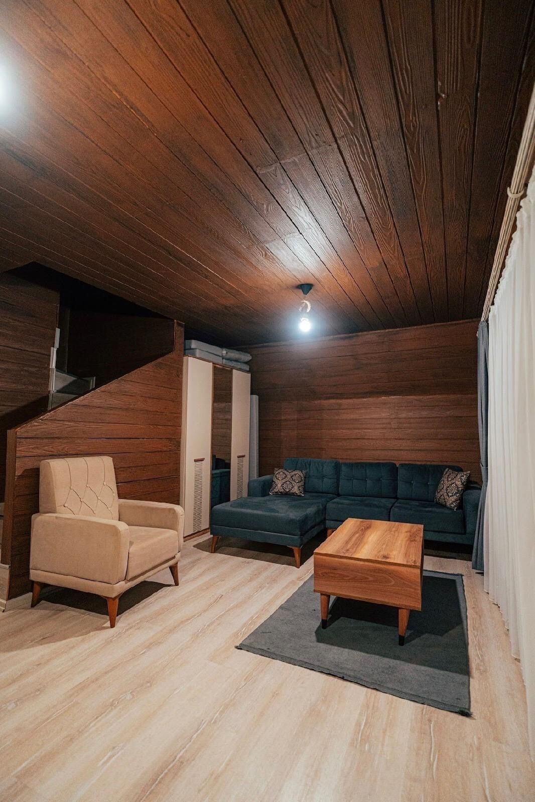 A cozy room with a wooden ceiling, a sofa, a chair, and a coffee table.