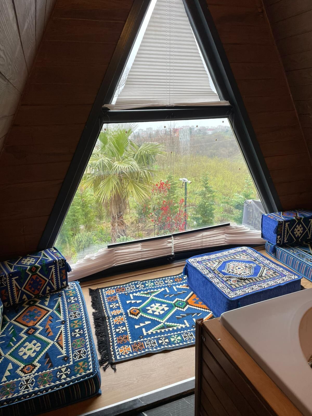 Um quarto com teto inclinado, uma janela grande e vista para o verde lá fora.