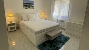 A bedroom with a bed, bedside lamps, a nightstand, a bench, a rug, a painting, and a window with curtains. - House for 4, just 3 min from marina and beach (Sari-Solenzara)