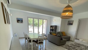 A spacious living area with a dining table, chairs, a sofa, and a large window. - House for 4, just 3 min from marina and beach (Sari-Solenzara)