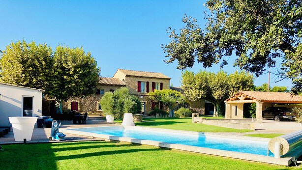 A swimming pool surrounded by a well-maintained lawn, stone buildings, and trees. - Bastide desRomarins (Cavaillon)