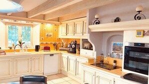 A kitchen with white cabinets, a built-in oven, and a dining area with a table and chairs. - Bastide desRomarins (Cavaillon)