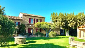 A stone house with a tiled roof, a well-maintained lawn, and a pergola with a white lantern. - Bastide desRomarins (Cavaillon)