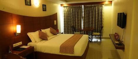 A hotel room with a large bed, a desk, a chair, a television, and a ceiling fan.