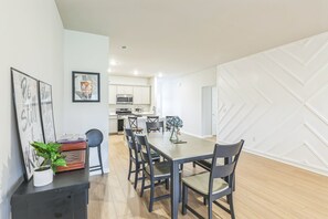 A modern dining area with a long table and chairs, a potted plant, and framed artwork on the wall. - Modern Nest - Huntsville Hideaway 3 Bedroom Home (Huntsville)