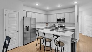 Une cuisine moderne avec des meubles blancs, des appareils en acier inoxydable et un îlot central doté de tabourets de bar.