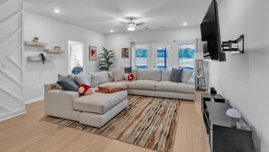 Un salon moderne avec un canapé d’angle, un téléviseur à écran plat et un ventilateur de plafond.