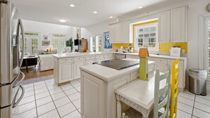 A modern kitchen with white cabinetry, a central island, and a dining area with a table and chairs. - Sunny Days 5 Bedroom Home (Georgetown)