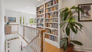 A staircase with white balusters leading to a landing, a large bookshelf filled with books, and a potted plant. - Sunny Days 5 Bedroom Home (Georgetown)