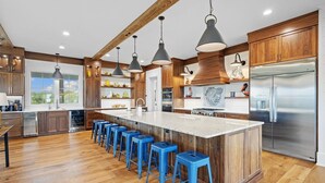 Een moderne keuken met houten kastjes, een roestvrijstalen koelkast en een centraal kookeiland met blauwe krukken.