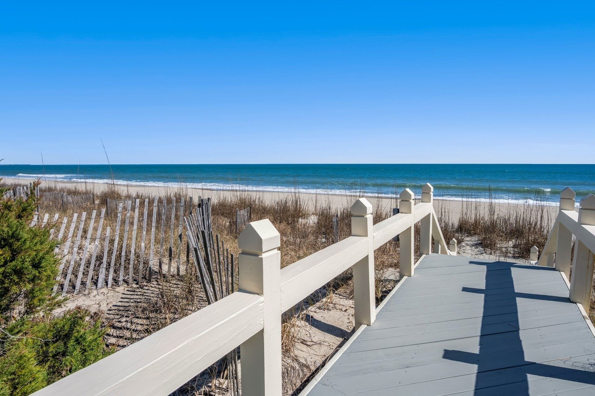 A wooden boardwalk leading to a beach with a clear blue sky.