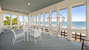 En takförsedd uteplats med vita möbler i rotting, en hängmatta och stora fönster med utsikt över havet.