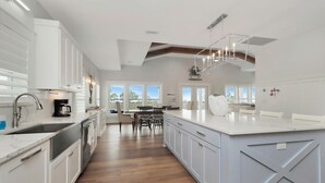 A modern kitchen with white cabinetry, a central island, and a dining area with a view. - ☀️Steps to Beach | Great Decks | Golf Cart Included | Home Away From Home☀️ (Port St Joe)