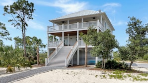 A two-story beachfront house with a balcony, a staircase leading to the upper level, and a sandy driveway. - ☀️Steps to Beach | Great Decks | Golf Cart Included | Home Away From Home☀️ (Port St Joe)